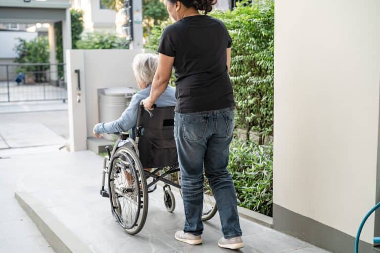 7 ADA Ramp Requirements Every California Property Owner Must Know 6 Person pushing elderly woman in wheelchair up a concrete ADA ramp near residential building