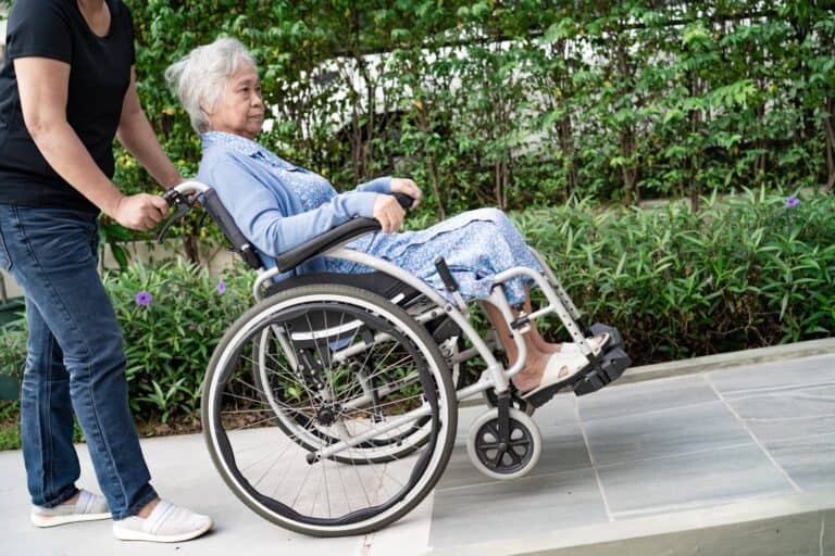 7 ADA Ramp Requirements Every California Property Owner Must Know 7 Senior in wheelchair being guided down a compliant ramp with proper slope and edge