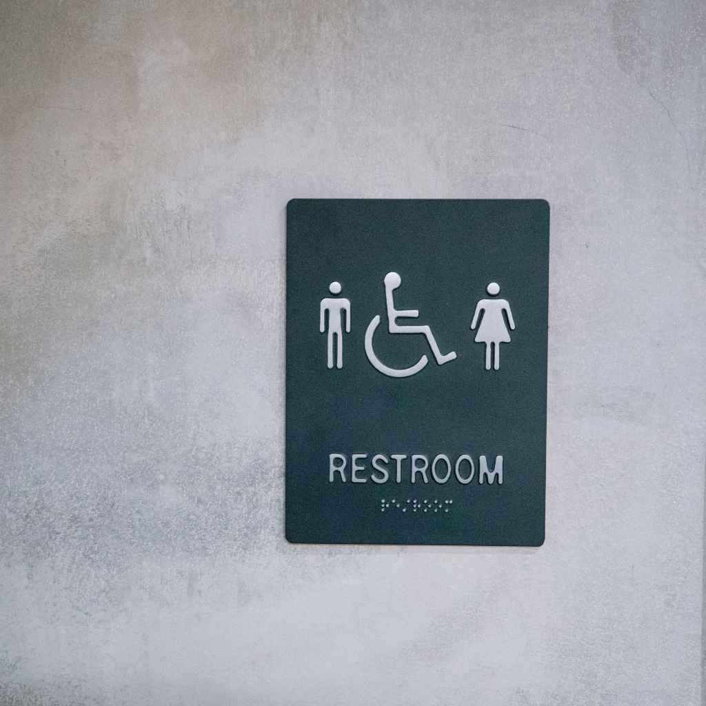 Make Your San Diego Restroom ADA Compliant | Step-by-Step Upgrade Guide 1 A black tactile restroom sign with male, female, and wheelchair symbols mounted on a light gray wall, representing ADA-compliant restroom signage required under California Title 24 and the 2010 ADA Standards