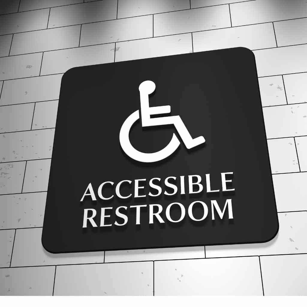 an accessible restroom sign mounted on a tiled commercial wall, showing the International Symbol of Accessibility used in CASp evaluations of restroom compliance.