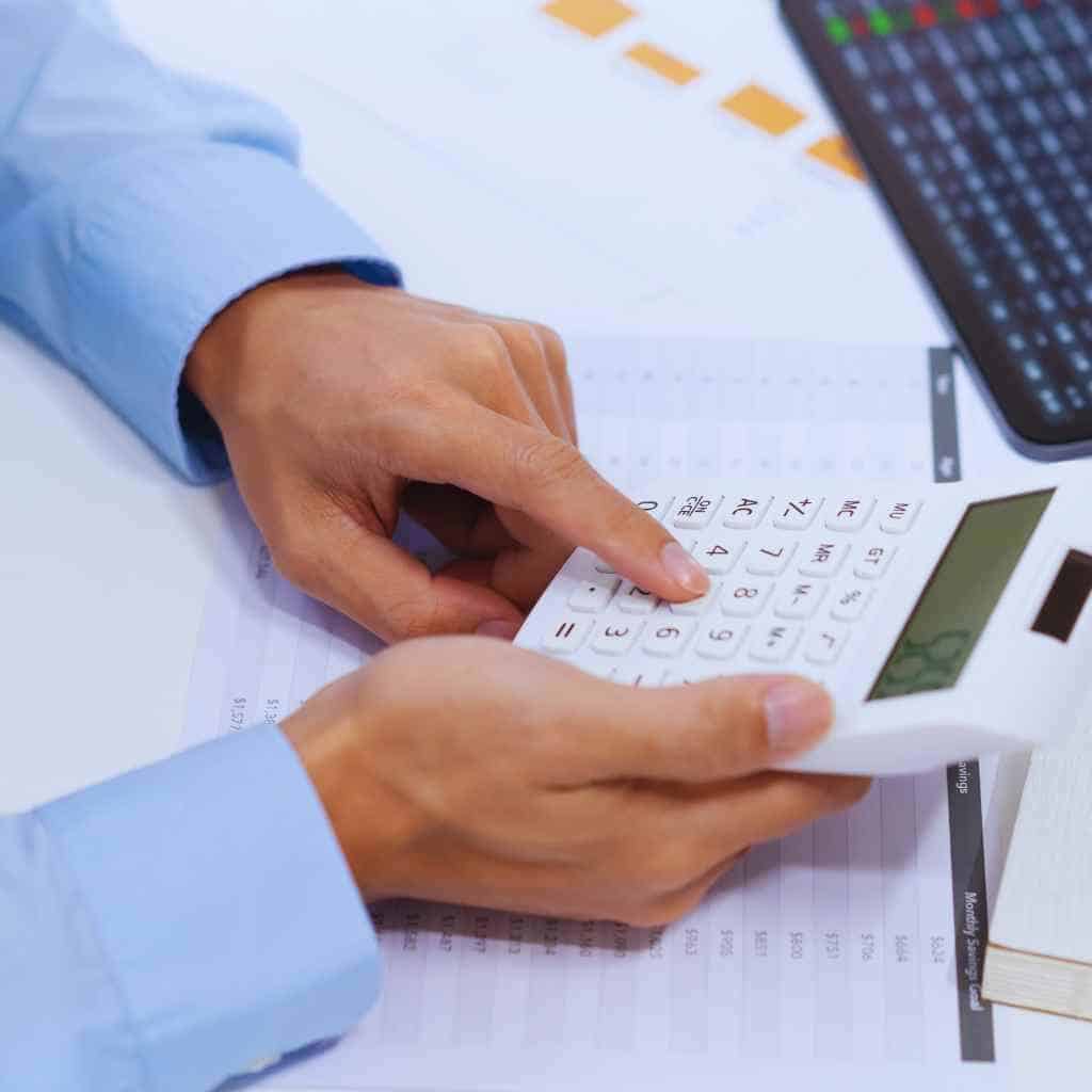 Person reviewing cost estimates on a calculator while analyzing documents, illustrating how CASp inspection pricing is calculated for California ADA and Title 24 compliance.