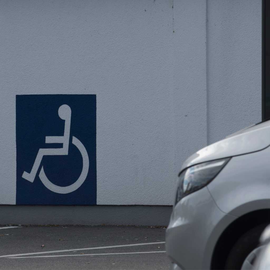 Painted accessibility symbol on an exterior building wall beside a parking area, illustrating elements CASp inspectors review when assessing accessible routes and parking compliance.