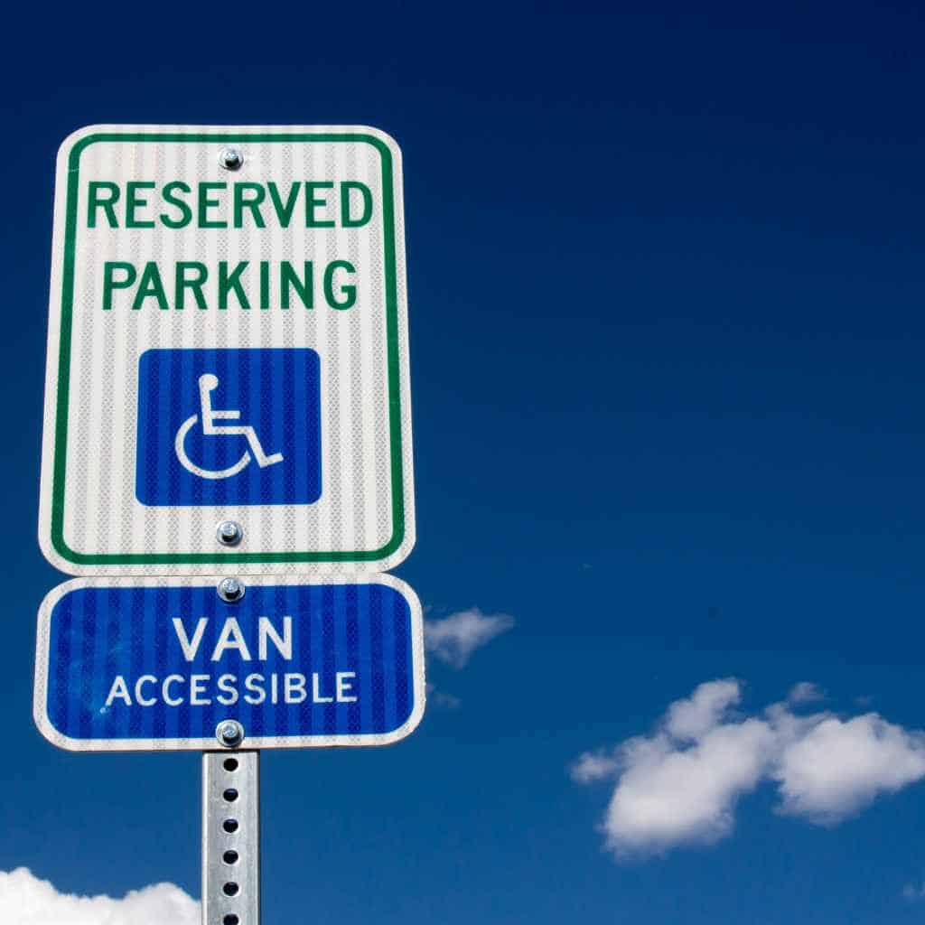 A reserved parking sign with the wheelchair symbol and a van-accessible designation, photographed against a clear blue sky, illustrating ADA and California Title 24 parking requirements that affect CASp inspection costs.