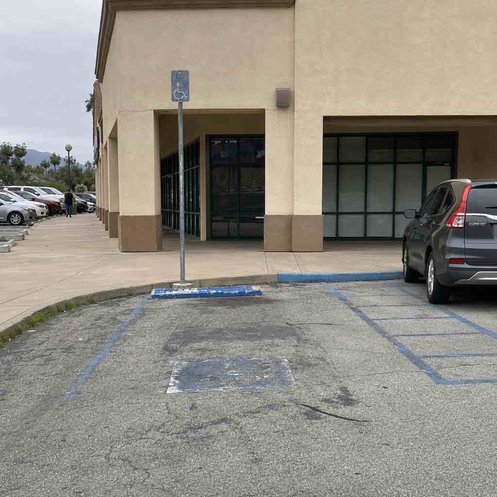 California commercial parking lot with faded accessible parking signage and worn blue curb paint visible from street distance